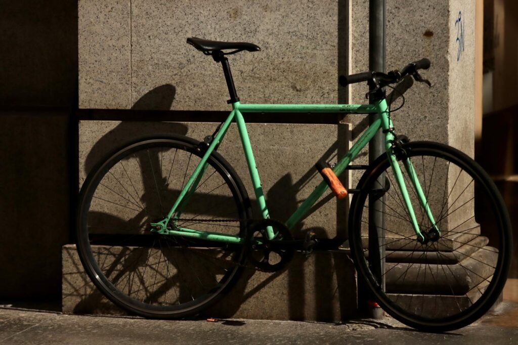 A city commuter bike locked to a sidewalk rack with the frame and rear wheel secured by a U-lock