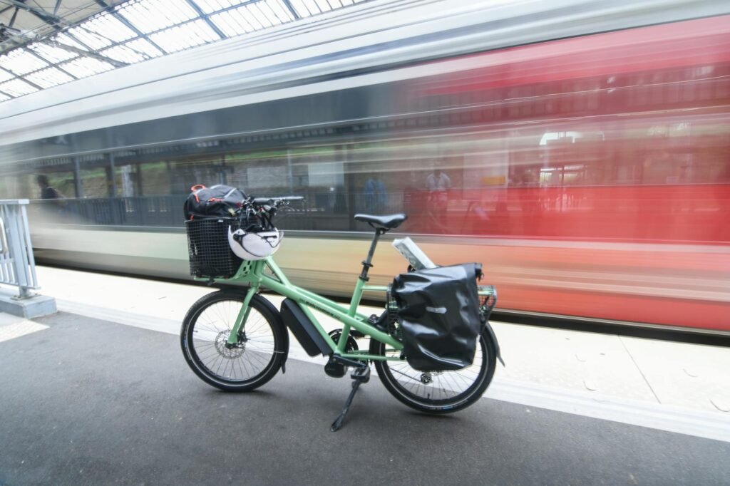 A commuter e-bike locked to a city bike rack with a pannier bag and grocery tote