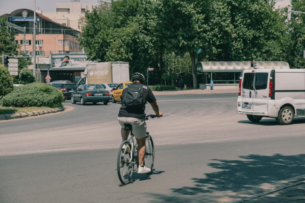 A cyclist waiting at a city intersection in a clear lane position near parked cars