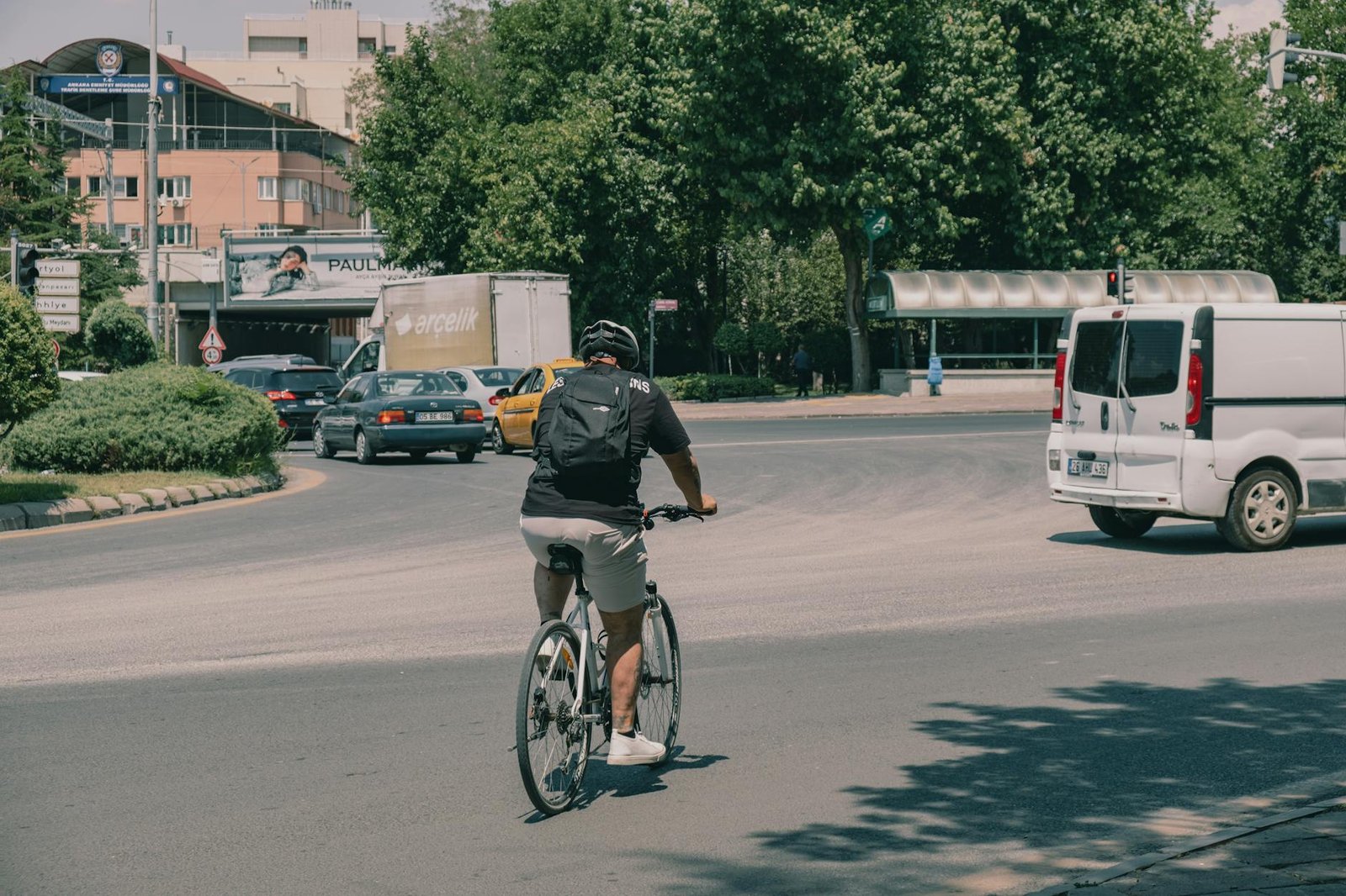 A cyclist waiting at a city intersection in a clear lane position near parked cars