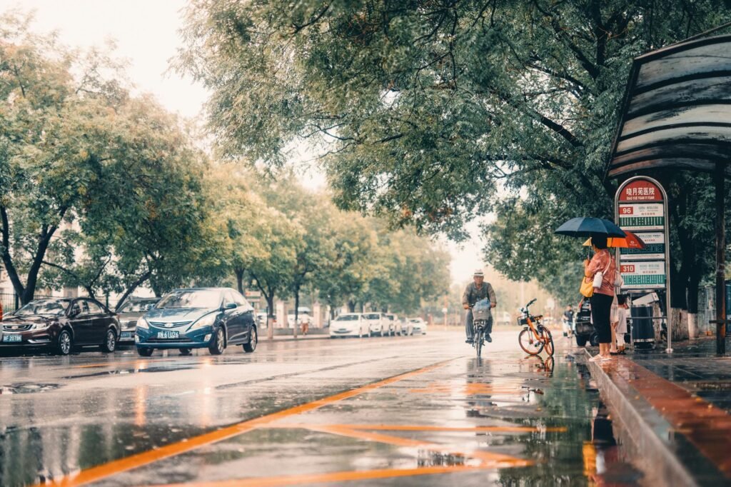 A wet urban bike lane on an overcast day with visible lane markings and light traffic.