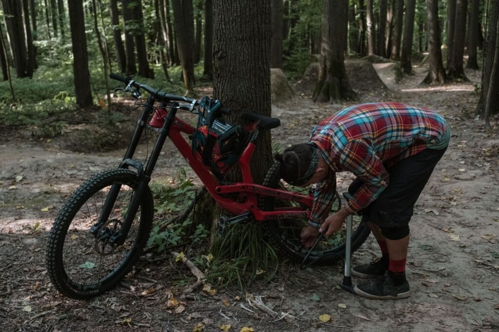 A simple home bike-maintenance setup with a floor pump, chain lube, rag, patch kit and spare tube beside a commuter bike.